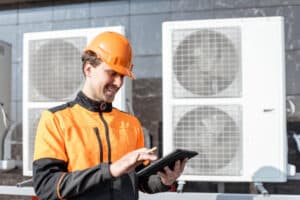 Workman servicing air conditioning or heat pump with digital tablet